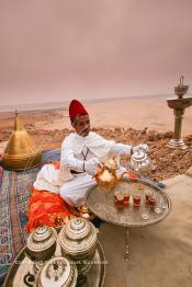 Image du Maroc Professionnelle de  Un marocain traditionnellement vêtu serve du thé à la menthe aux invités du grand Moussem de Tan Tan. Installée avec ses plateaux sur les hauteurs de la plage Chbika au environ de Tan Tan. Le Moussem est une sorte de foire annuelle, à la fois économique, culturelle et sociale. Il est classé par l'Unesco en 2005 comme patrimoine immatériel humain mondial. Chaque année la majorité des tribus et des grandes familles nomades du désert se retrouvent sur un site désertique pour célébrer ce grand Moussem où  danse, chants, course de chameaux et fantasia font partie des festivités. , Samedi 18 septembre 2004, ((Photo / Abdeljalil Bounhar)